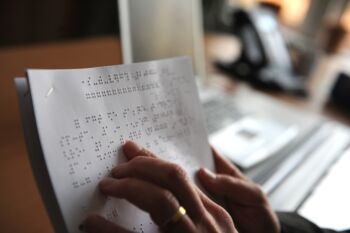 Lesende Finger ertasten auf einem Blatt Papier die geprägte Braille-Schrift